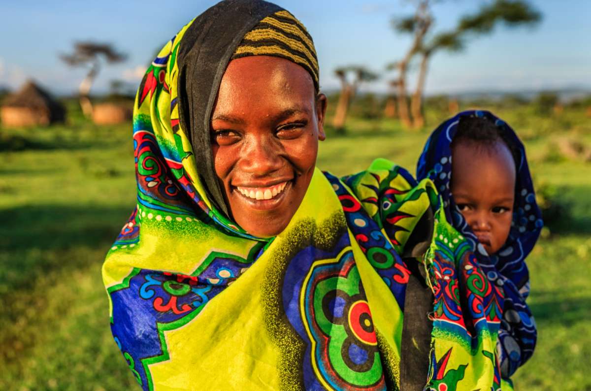 Local woman with child in traditional clothing in rural Africa, smiling in a natural outdoor setting 