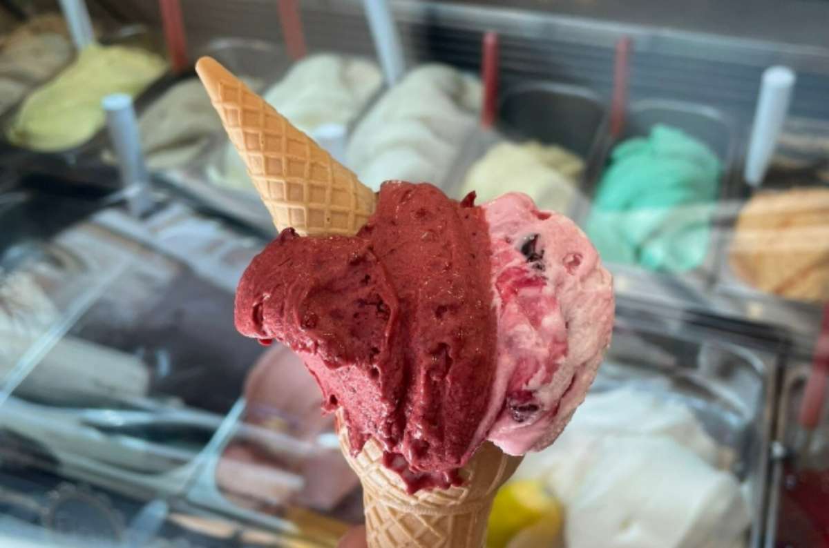 A cone with two scoops of Italian gelato held in front of a gelateria display case, Facts about Italian food
