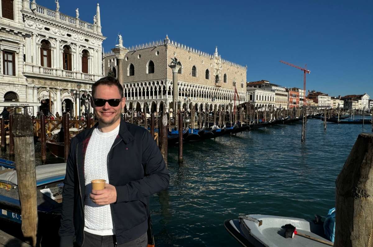 Tourist by the canal in Venice, Italy, holding a to-go coffee, photo by Next Level of Travel