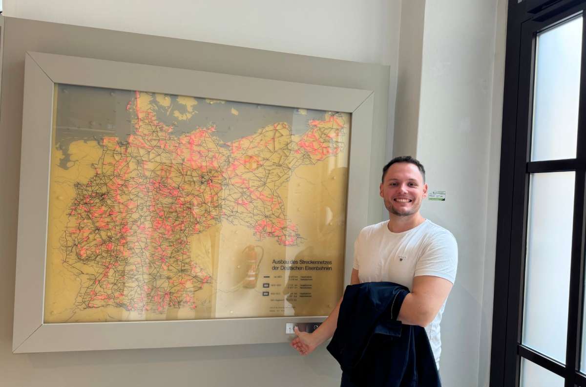 A man smiling and pointing at an interactive illuminated map showing the expansion of the German railway network, displayed inside German Railway Museum, photo by Next Level of Travel
