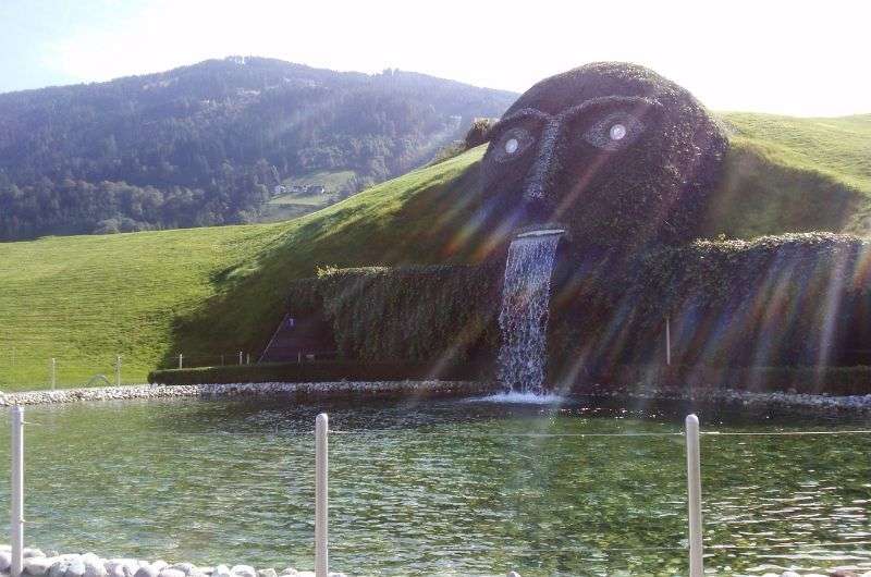 Giant grass-covered head sculpture with crystal eyes and a waterfall mouth at Swarovski Crystal Worlds, Austria