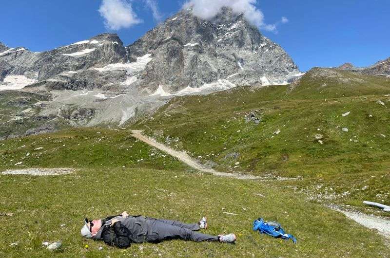 A hiker laying on his back in the grass in the valley under the Matterhorn, Italy, photo by Next Level of Travel