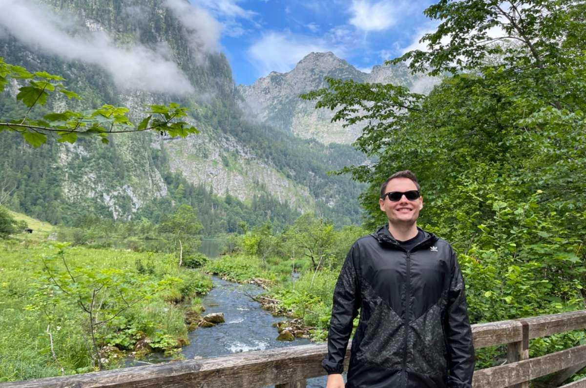 A tourist in sunglasses smiling while standing on a wooden bridge in nature near the Eagle’s Nest in Germany, photo by Next Level of Travel