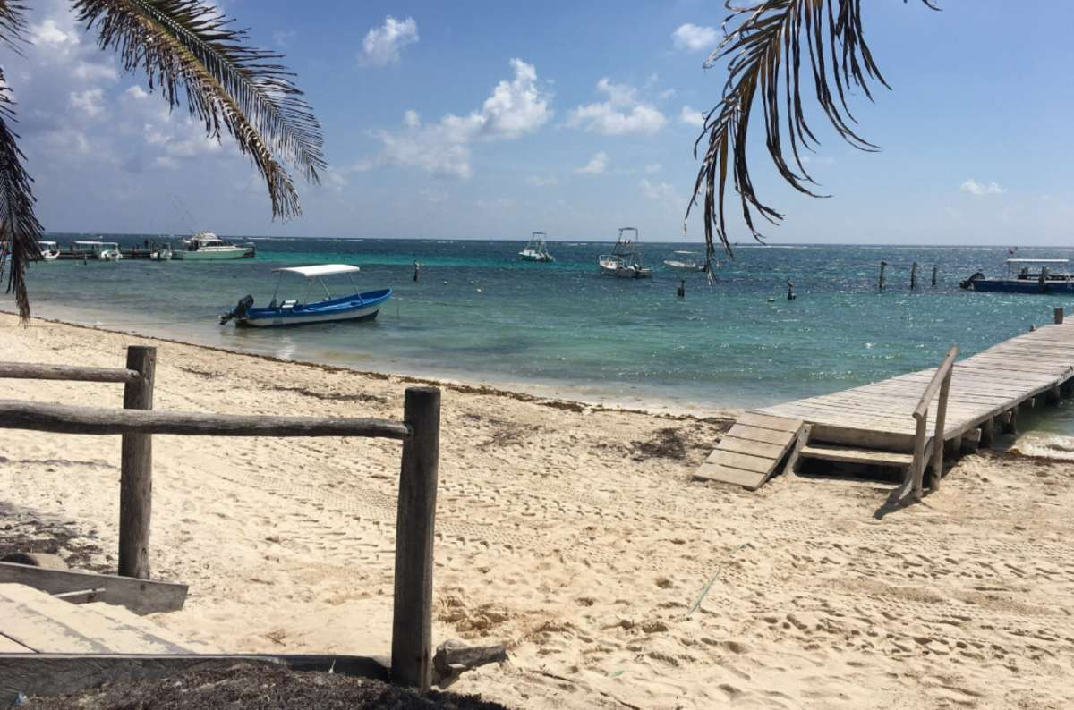 Quiet beach in Puerto Morelos, Mexico, with white sand, wooden pier, small boats, and the turquoise Caribbean Sea