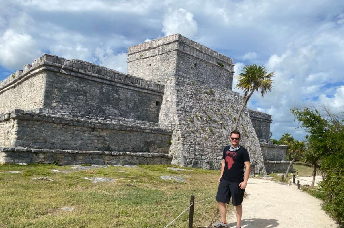 Stone ruins of the Tulum archaeological site on the Caribbean coast in Tulum, Mexico, with ancient Mayan structures and male tourist in front on a sandy path, photo by Next Level of Travel