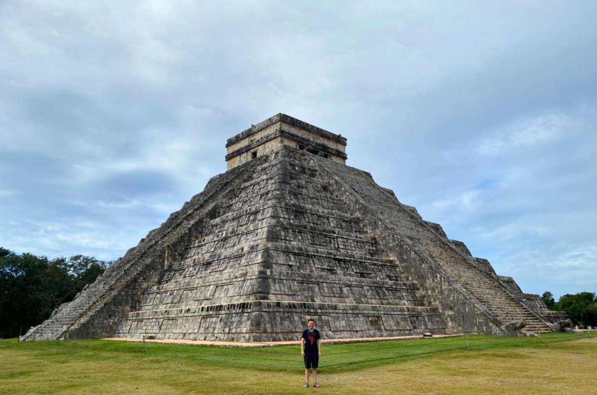 Tourist male standing in front of El Castillo pyramid at the Chichen Itza archaeological site in the Yucatan Peninsula, Mexico, on a warm day, photo by Next Level of Travel