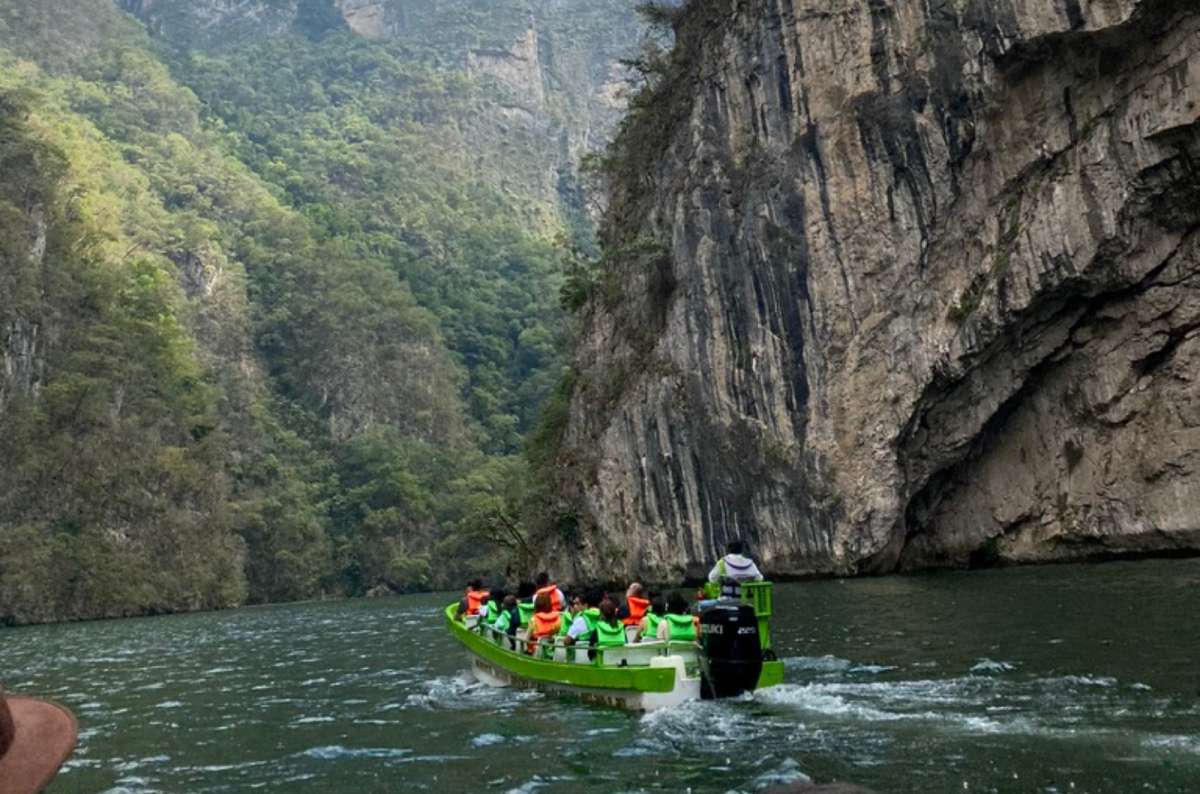 a boat filled with tourists taking a ride in the Sumidero Canyon, with the high walls of the canyon and the beautiful water visible in the frame, Mexico, photo by Next Level of Travel