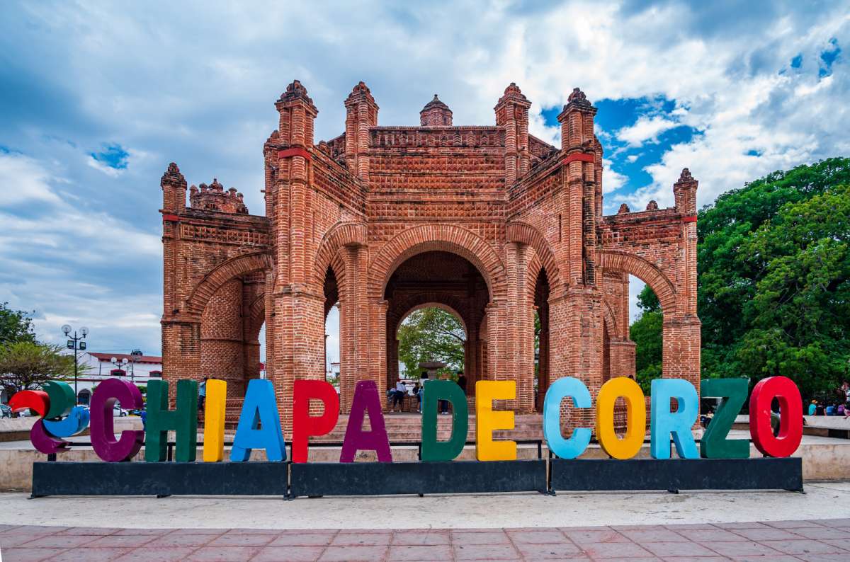 a photo from Chiapa de Corzo, showing a colorful sign with its name and a beautiful hollow decorative structure in the background, Mexico