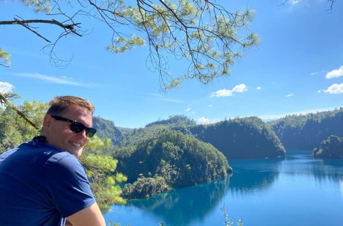 a photo of a tourist posing in front of the view at Lago Montebello, with colorful trees and  the crystal blue lake decorates the background, Mexico, photo by Next Level of Travel