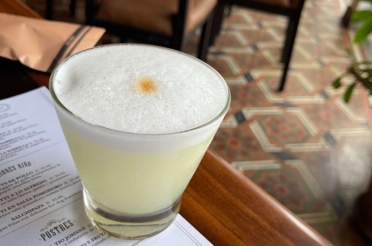 Pisco Sour in a glass on a wooden table, peruvian food and drinks, photo by Next Level of Travel