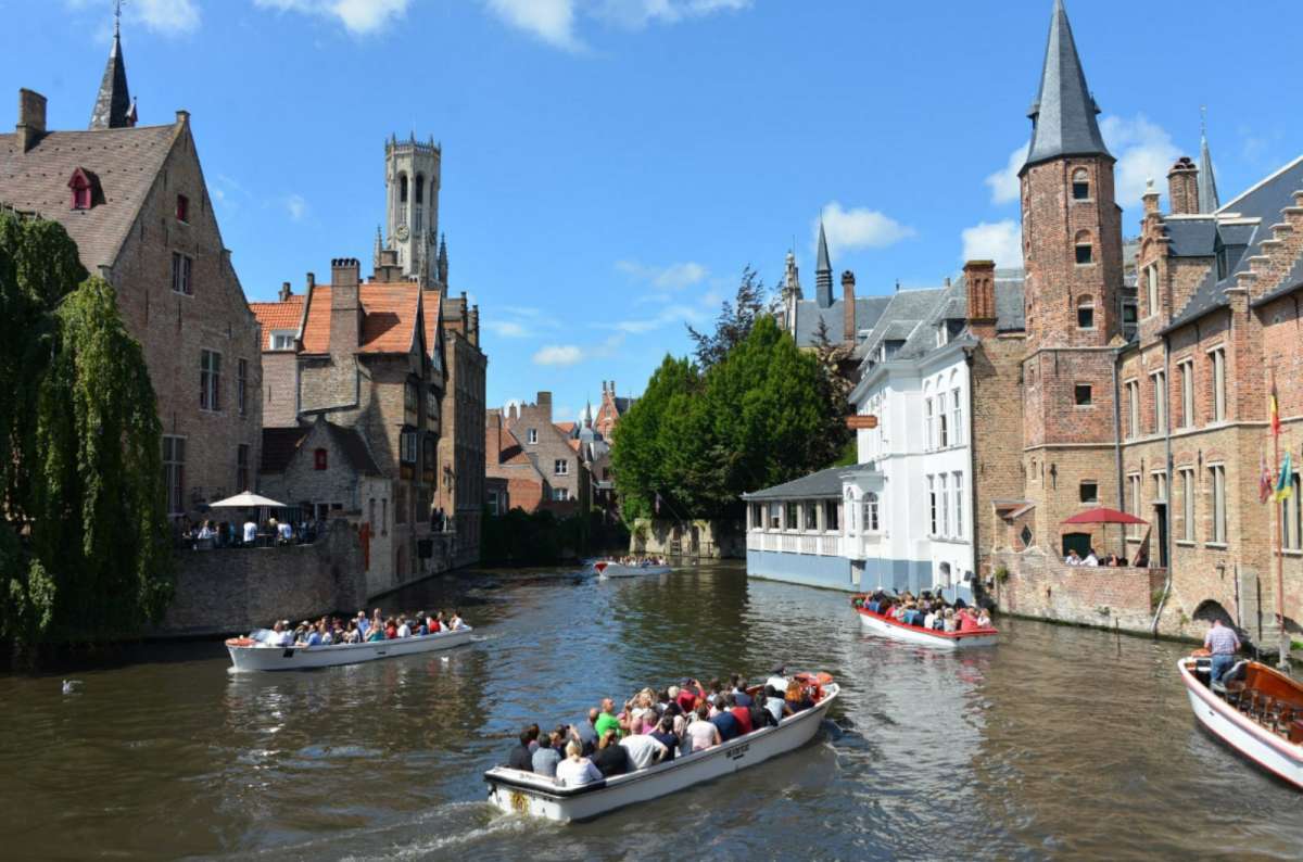 Boats full of tourists cruising the medieval canals of Bruges, Belgium, with Belfry of Bruges visible in the background