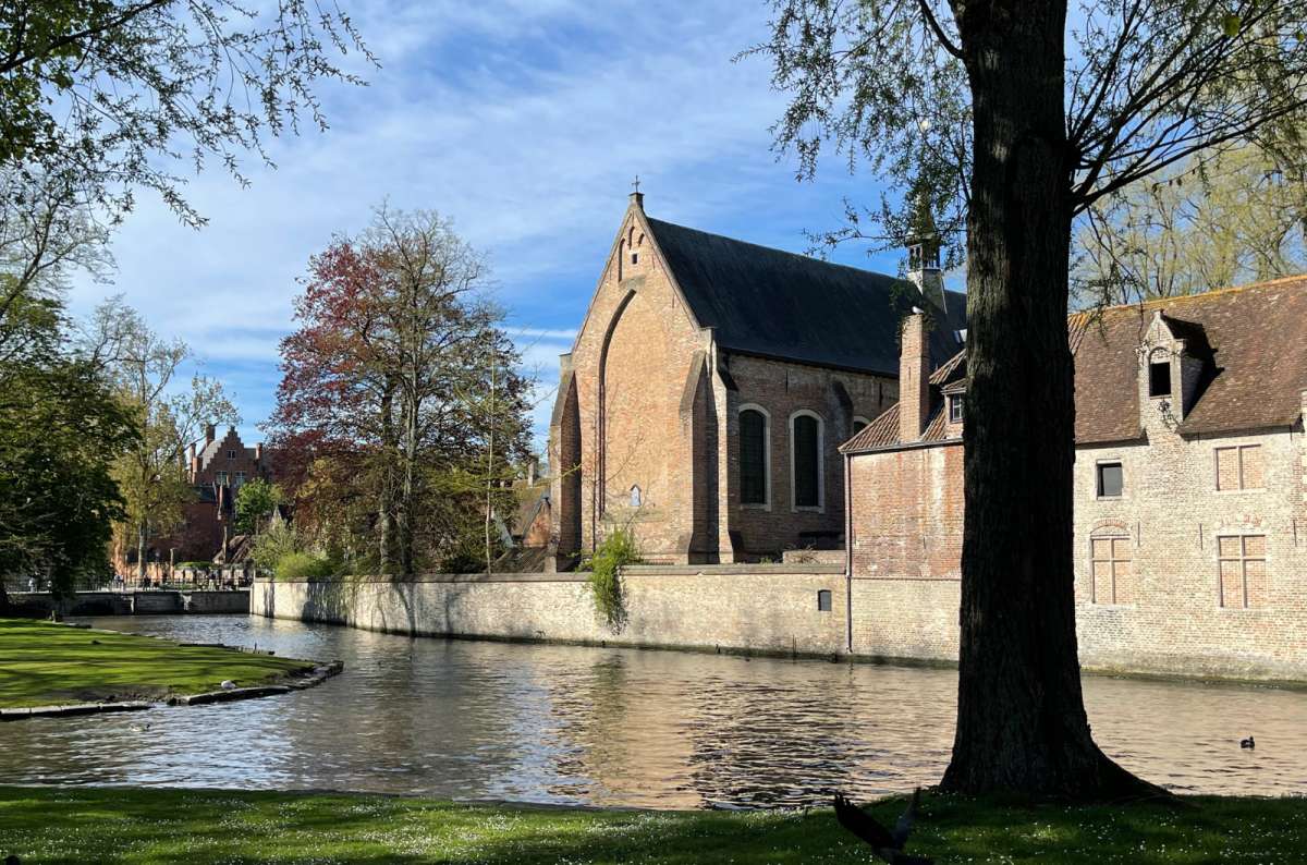 Peaceful canal scene in Bruges, Belgium, with historic brick buildings and a church surrounded by greenery, photo by Next Level of Travel