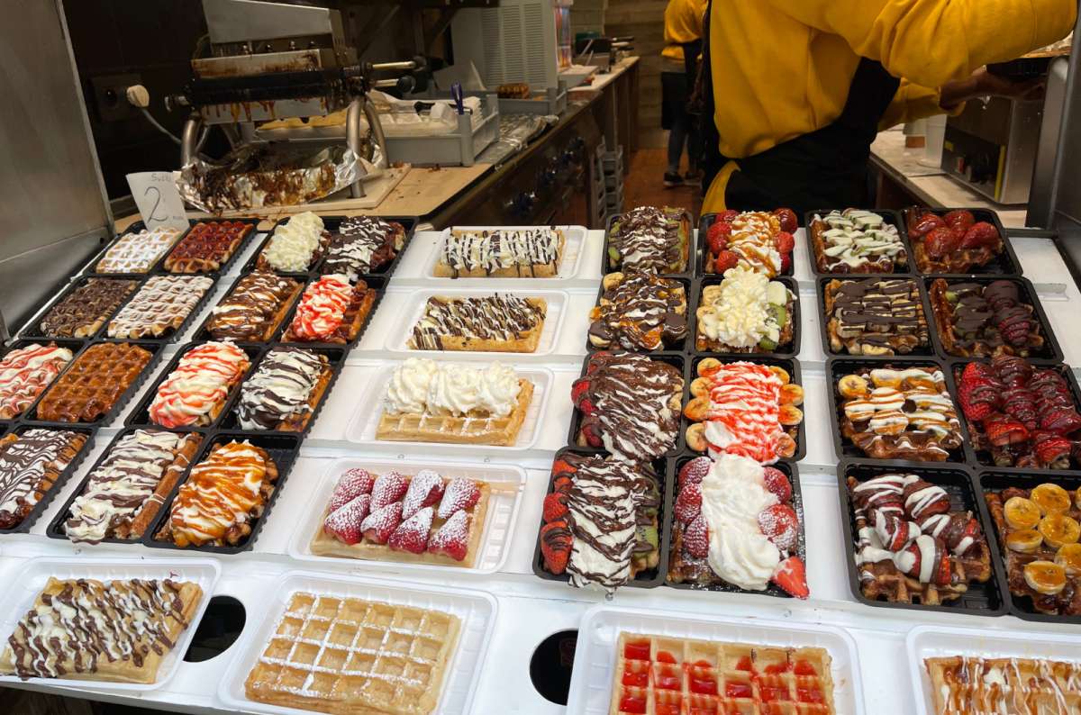 Assortment of colorful Belgian waffles topped with whipped cream, chocolate, and fruit in a waffle shop in Brussels, photo by Next Level of Travel