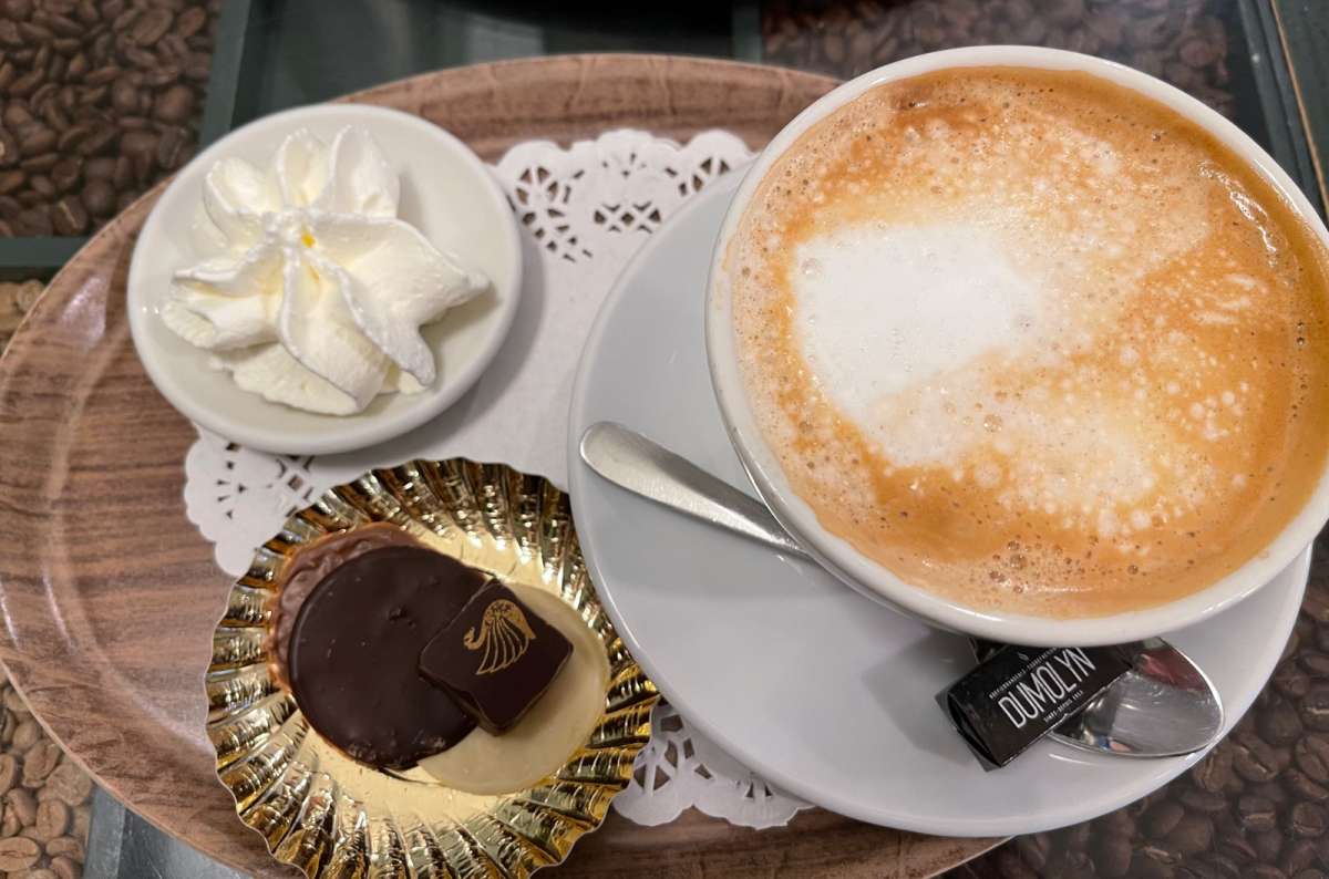 Cappuccino with whipped cream and Belgian pralines on a wooden tray, served in a Brussels café, photo by Next Level of Travel