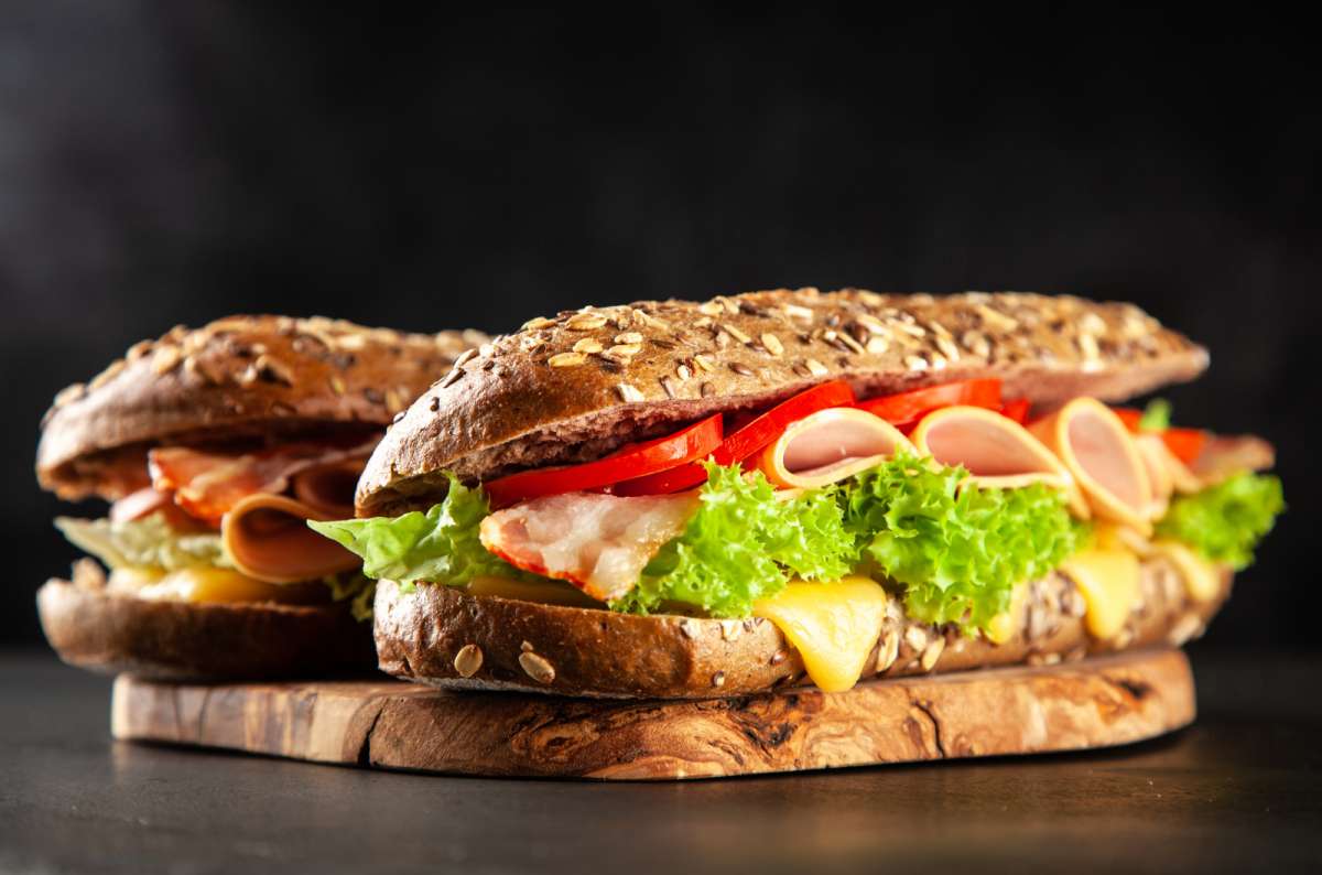 Close-up of two smoske sandwiches with ham, cheese, lettuce, tomato, and crusty multigrain bread