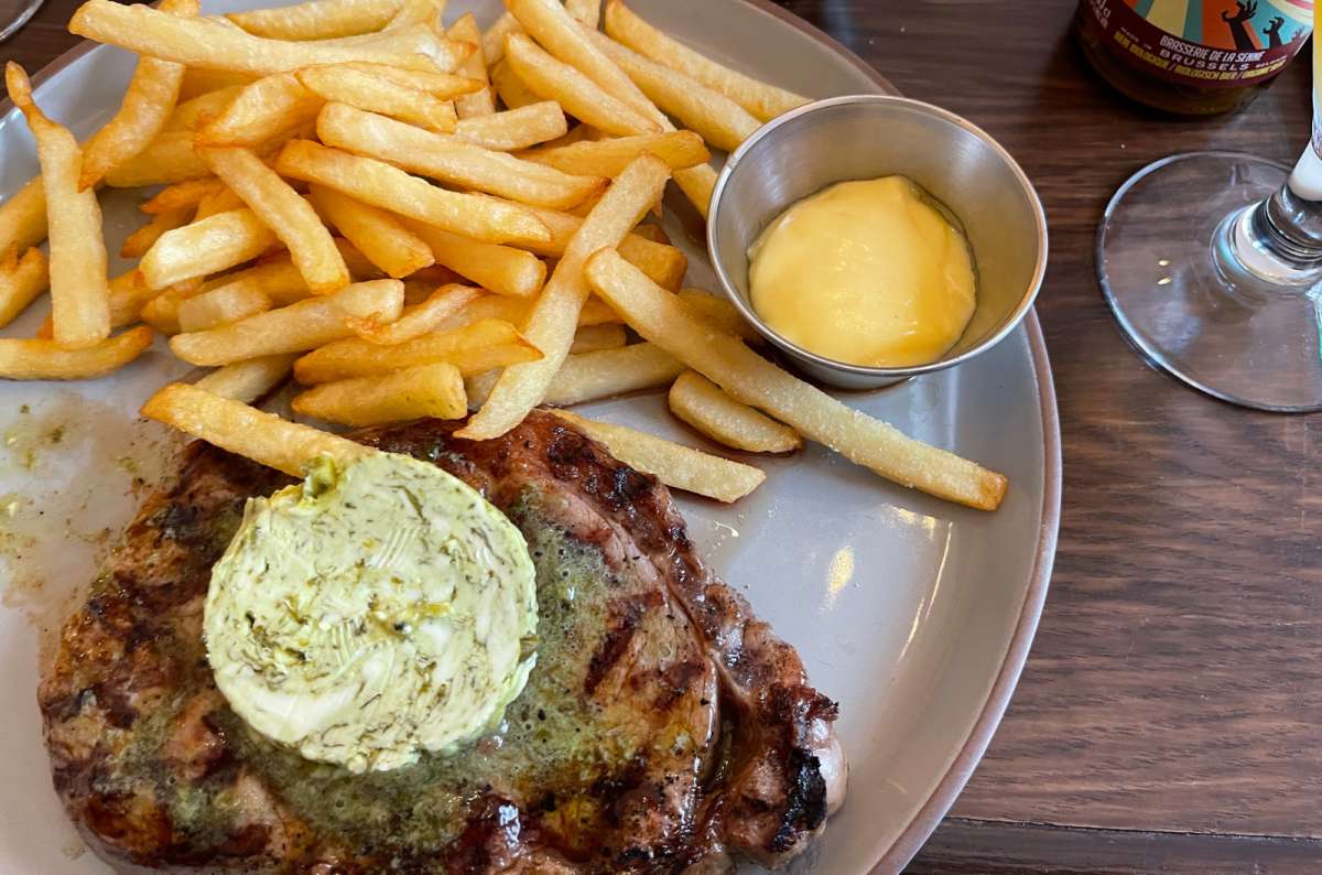 Grilled steak served with fries, herbed butter, and a side of mayonnaise on a plate in Brussels, photo by Next Level of Travel