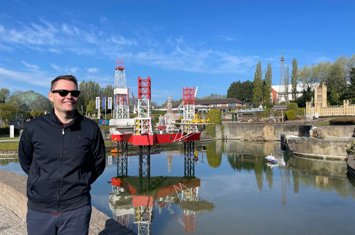 Man smiling in front of miniature oil rig and famous landmarks at Mini-Europe park in Brussels, Belgium, photo by Next Level of Travel