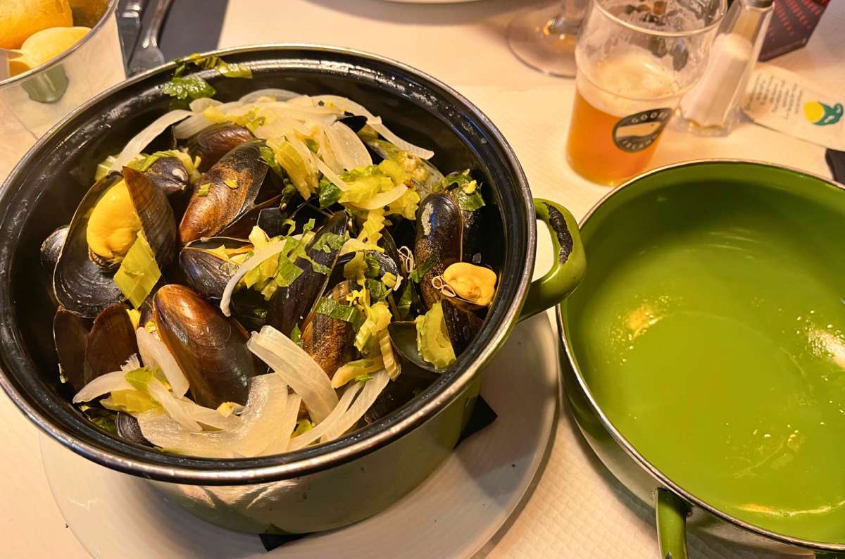 Traditional Belgian moules-frites—mussels cooked with onions, celery, and herbs in white wine sauce, served in a green pot, photo by Next Level of Travel
