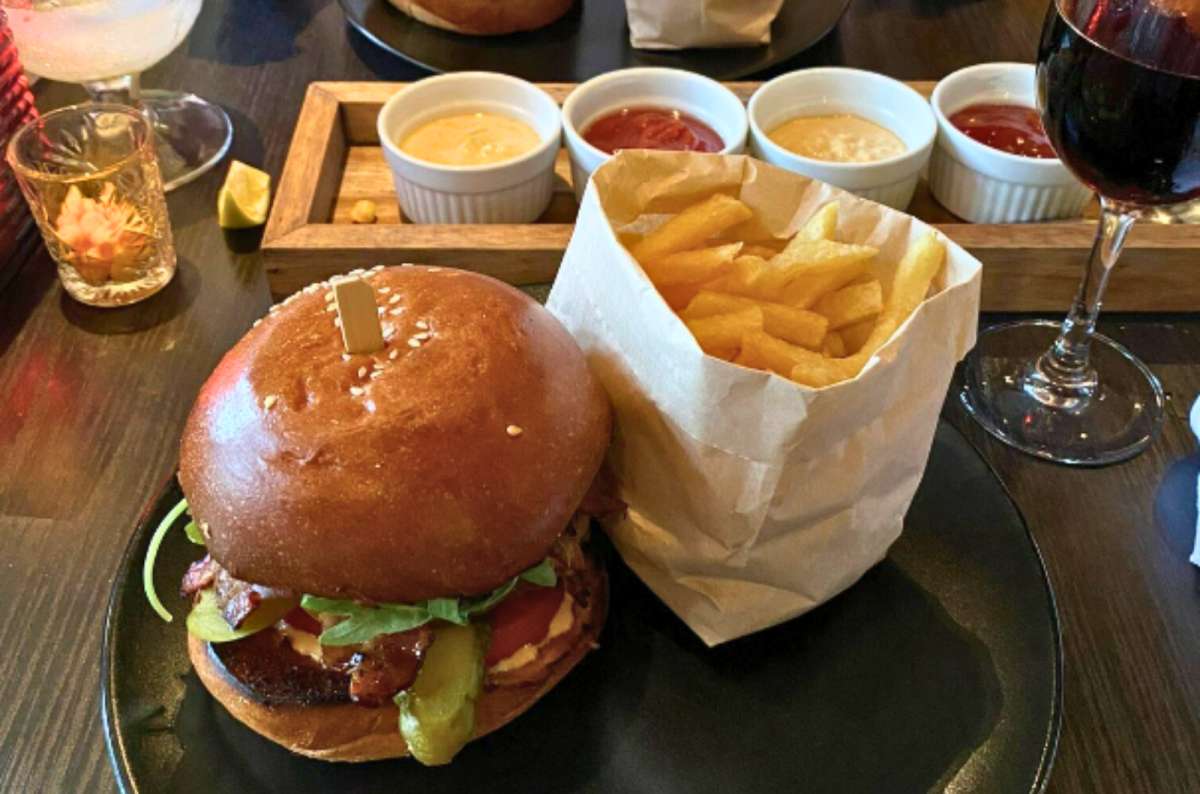burger with pickles, greens, and fries served with dipping sauces and wine at ‘t Koningshuis in Ghent, Belgium