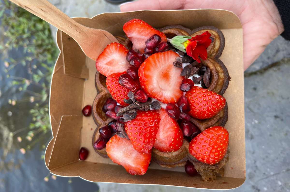 Close-up of a heart-shaped Belgian waffle from Otto Waffle Atelier in Ghent, topped with strawberries, pomegranate seeds, cacao nibs, and edible flower, photo by Next Level of Travel