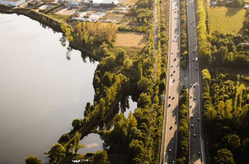 A highway in Belgium surrounded by trees and a lake