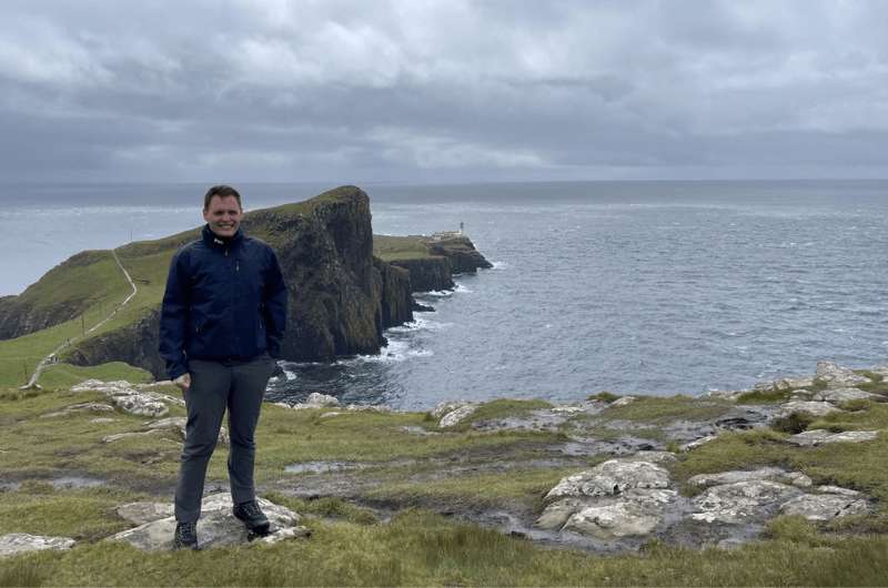 A tourist in front of the Neist Point Lighthouse view, Scotland