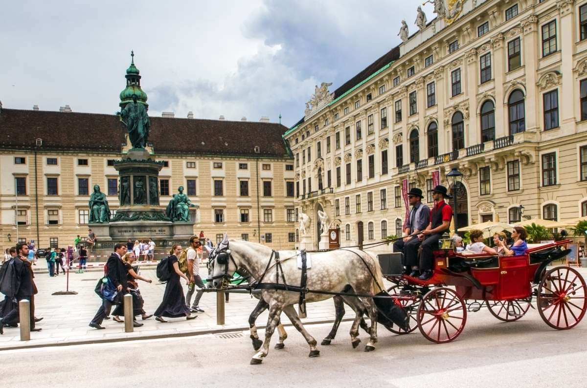 A traditional horse-drawn carriage carrying tourists passes through a historic square in Vienna, Austria