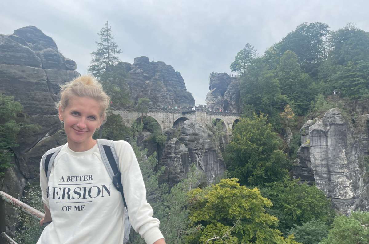 A woman in a white sweater posing in front of the Bastei Brücke, day trip from Dresden, Germany travel blog, photo by Next Level of Travel