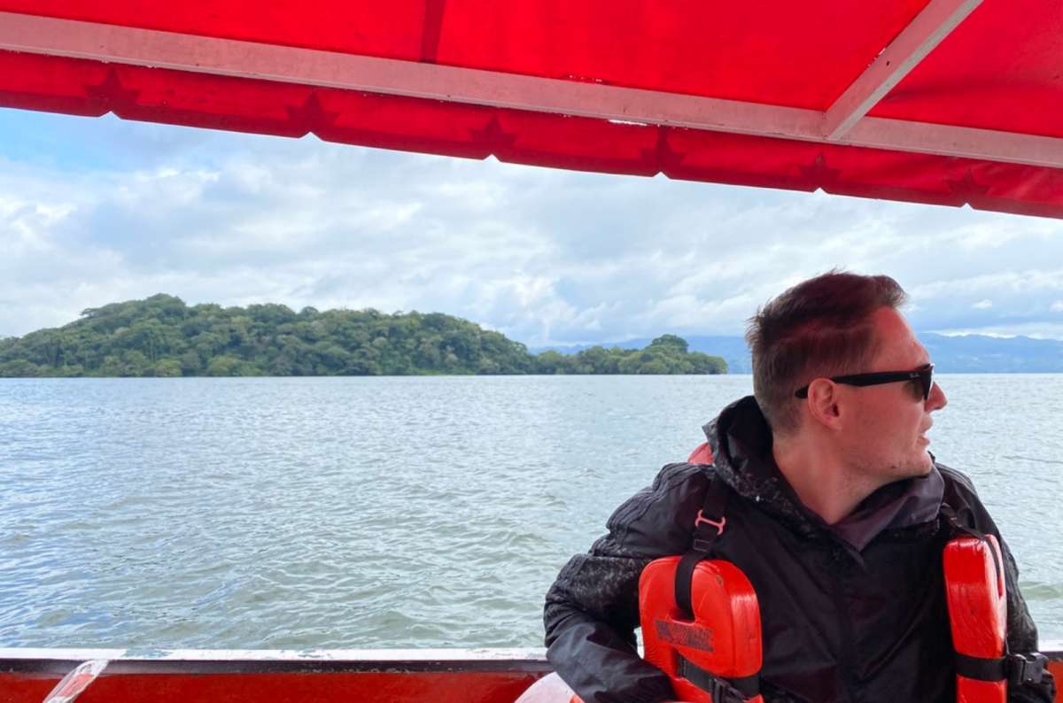 a photo of a tourist in a life vest on a boat crossing Laguna Catemaco with a forested island behind, Catemaco, Veracruz, Mexico, photo by Next Level of Travel