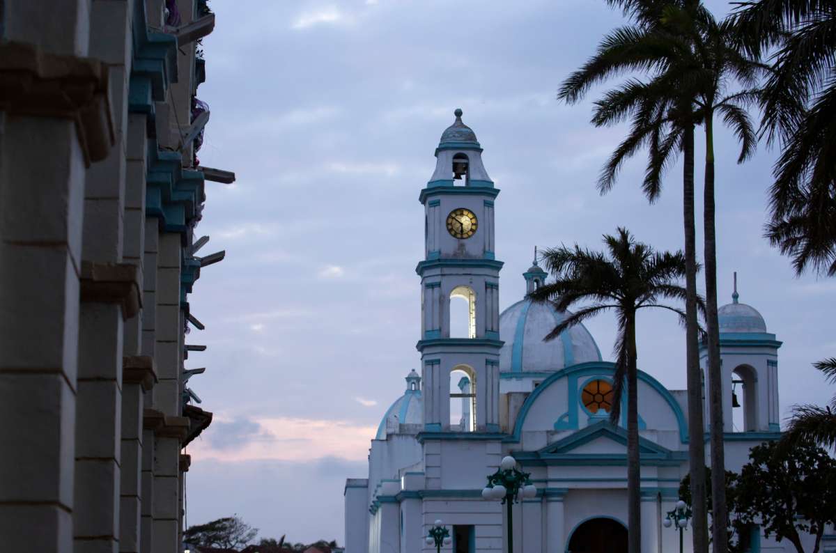 a photo of a white and blue colonial church with a clock tower and palm trees at dusk, Tlacotalpan, Veracruz, Mexico