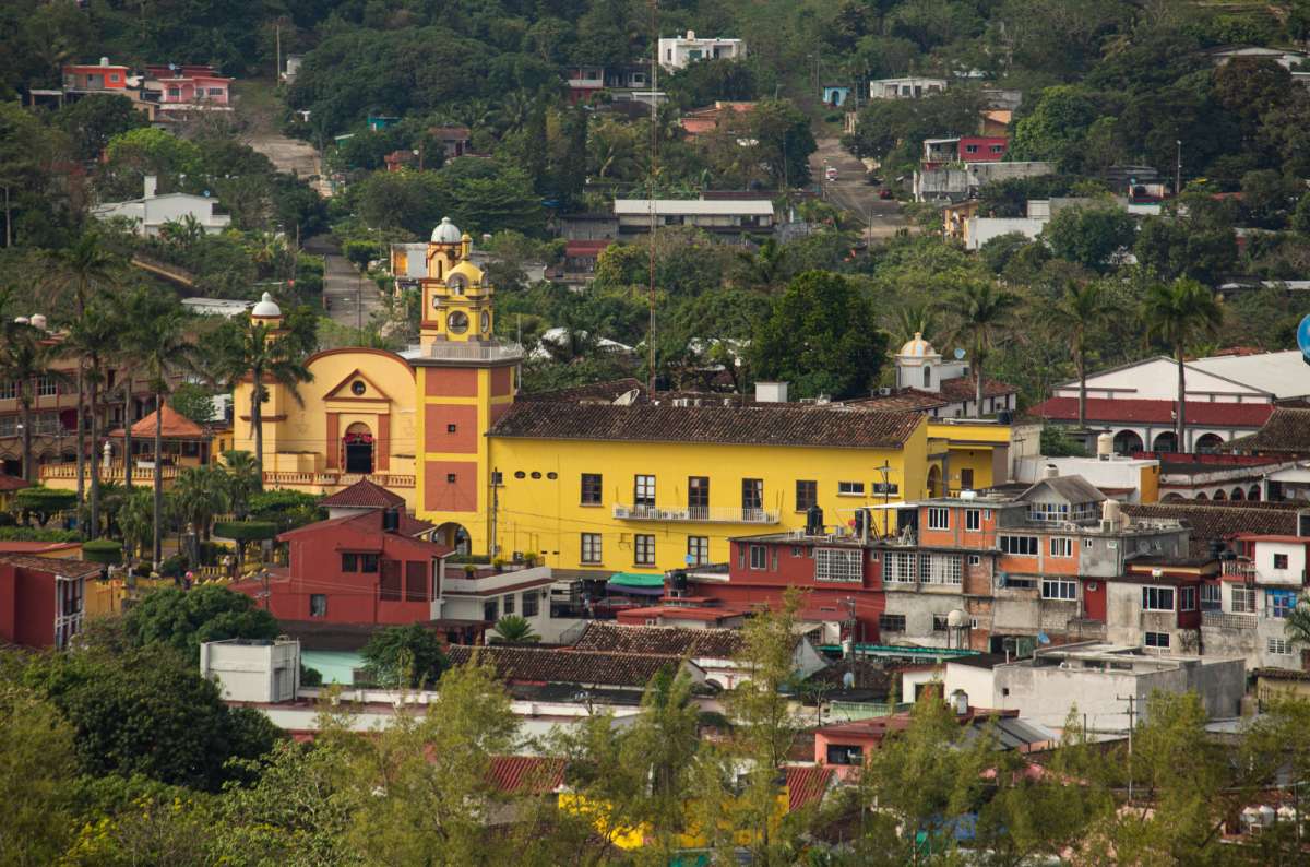 a photo of the yellow parish church and colorful houses of Santiago Tuxtla spread across lush green hills, Santiago Tuxtla, Veracruz, Mexico