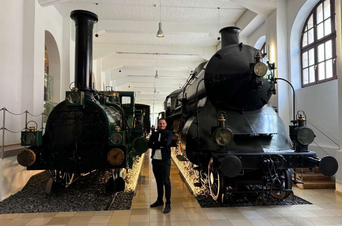 a tourist standing in front of two 19th century trains, Nuremberg Railway Museum, photo by Next Level of Travel