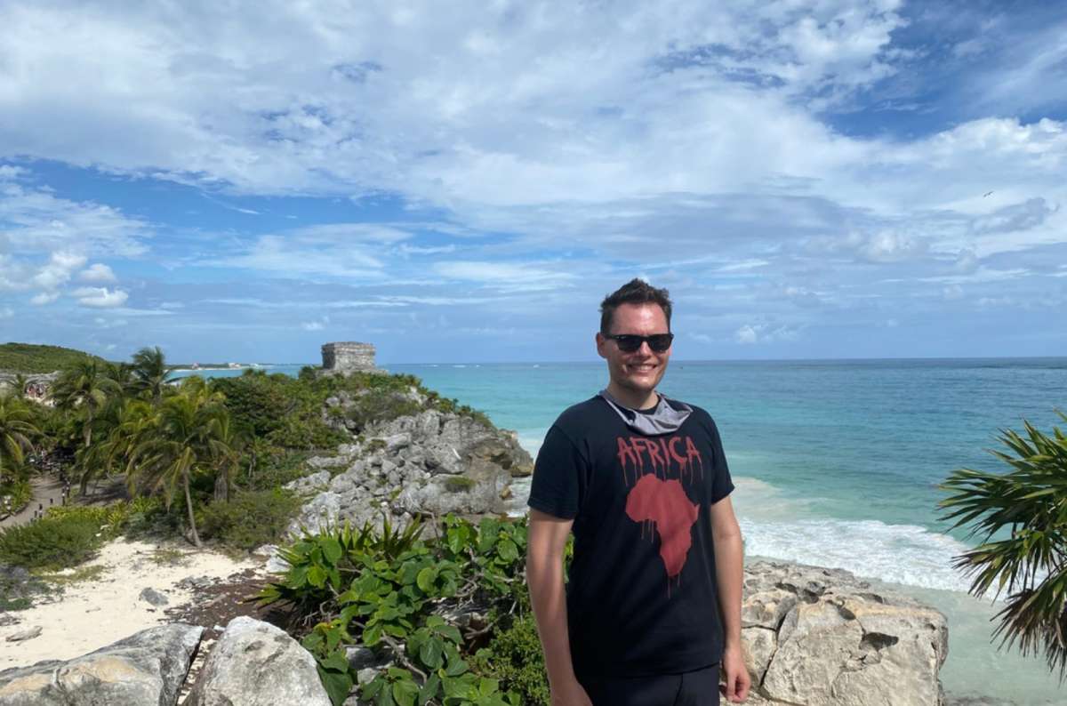 a tourist posing in Tulum with a beach and Mayan ruins in the background, Yucatán, Mexico, photo by Next Level of Travel