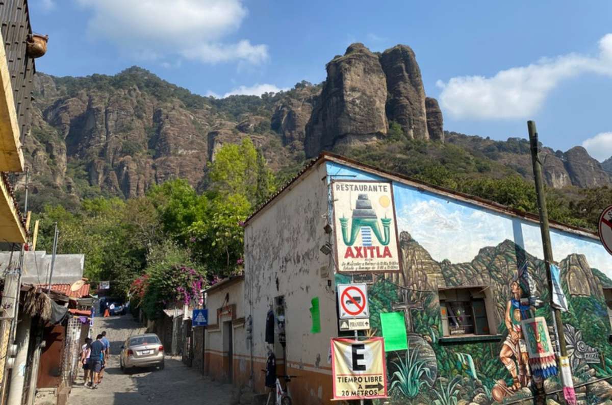 a photo of a cobblestone street in Tepoztlán leading up toward the cliffs of El Tepozteco, with a mural and the Axitla restaurant sign on the right, Tepoztlán, Mexico, photo by Next Level of Travel