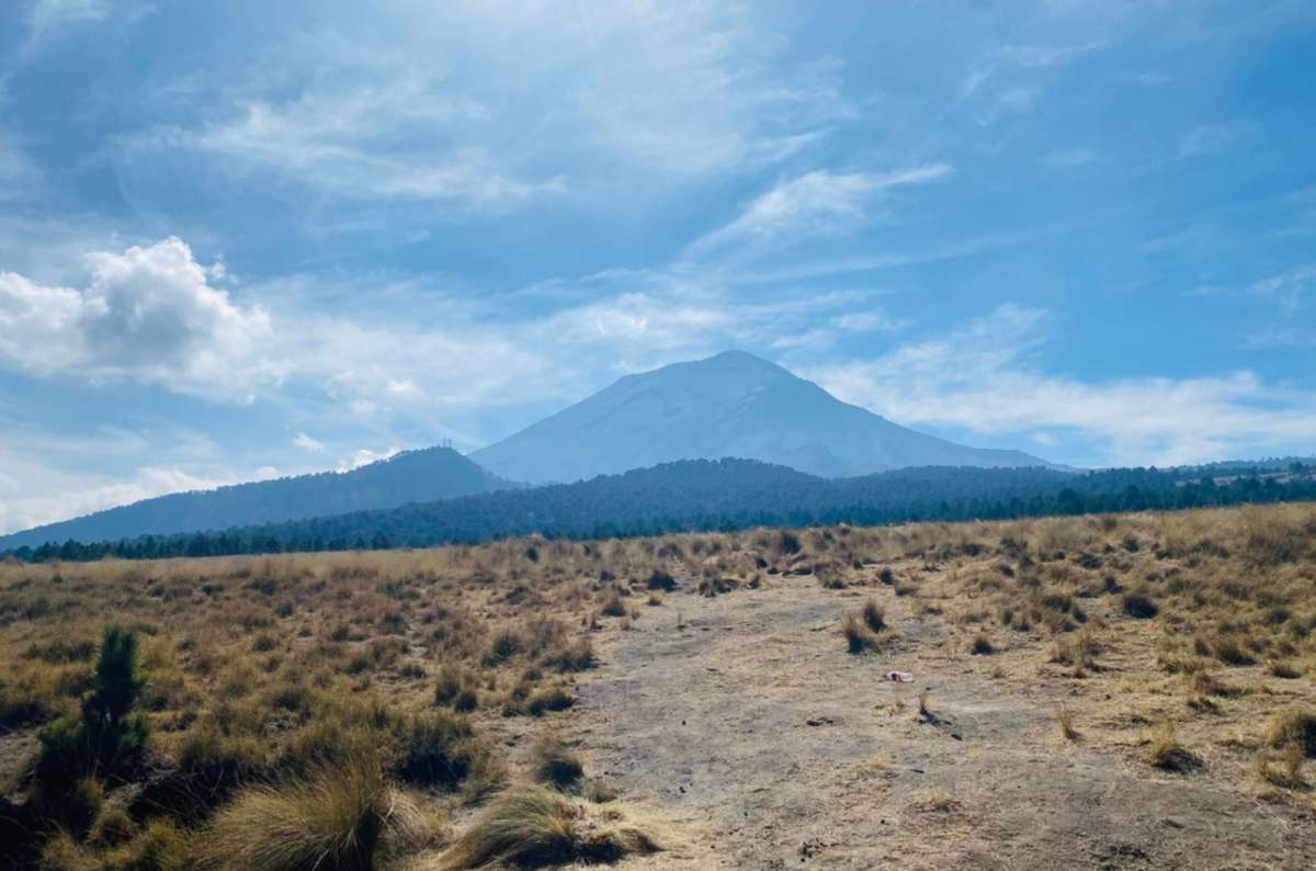 a photo of the Popocatépetl volcano rising over dry golden grassland under a blue sky, Mexico, photo by Next Level of Travel