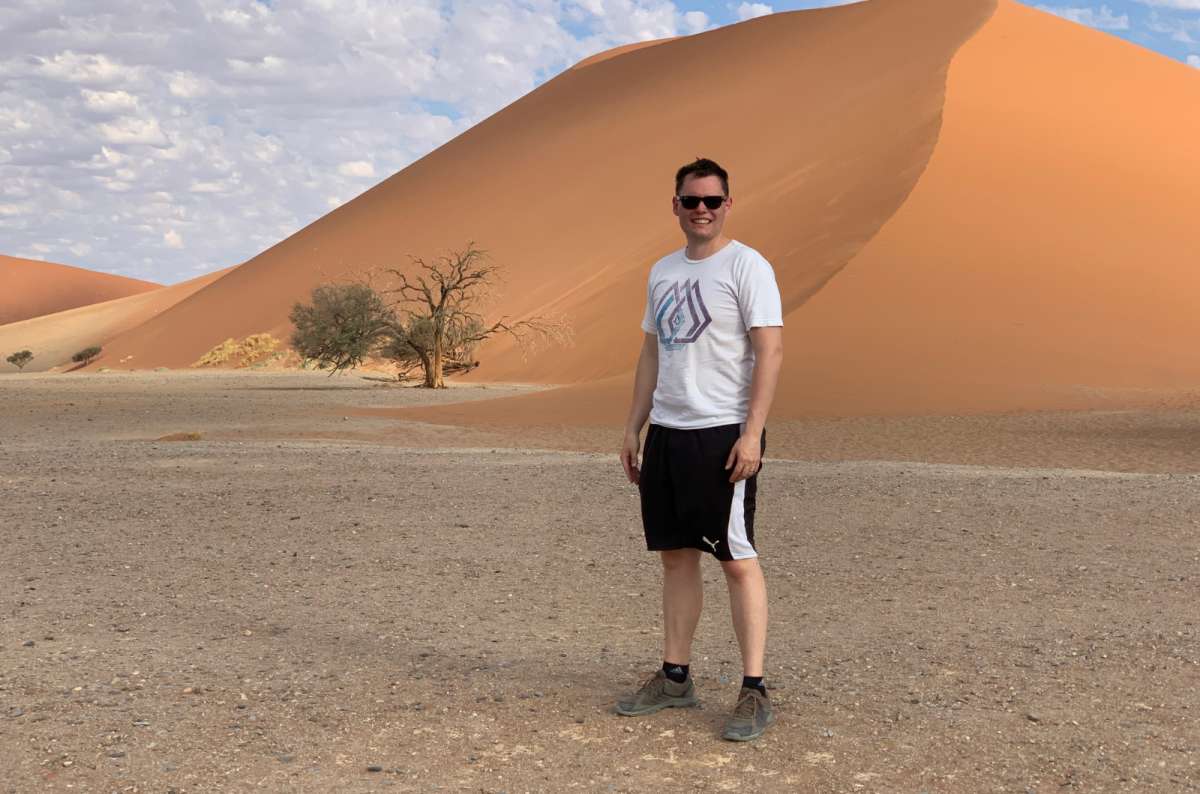 a photo of a tourist standing in front of the towering red sand dunes at Sossusvlei in Namibia, photo by Next Level of Travel