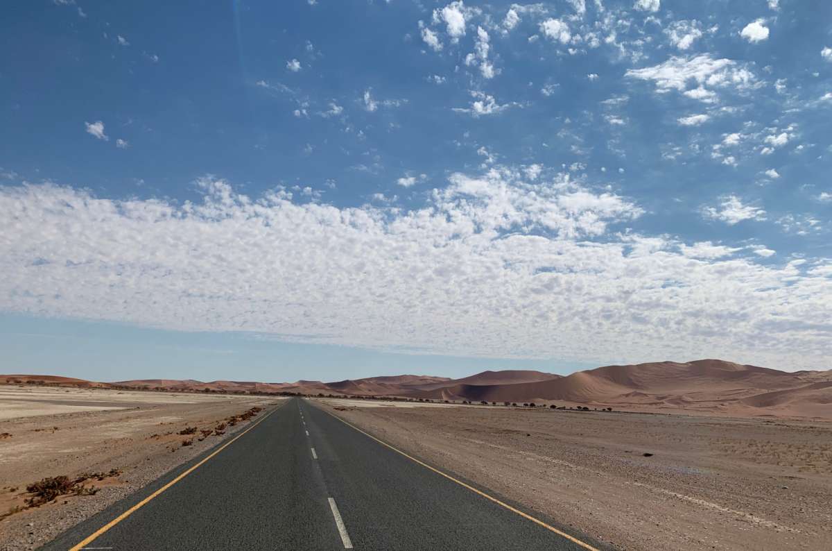 a photo of an empty paved road cutting through the Namib Desert near Sossusvlei in Namibia, photo by Next Level of Travel