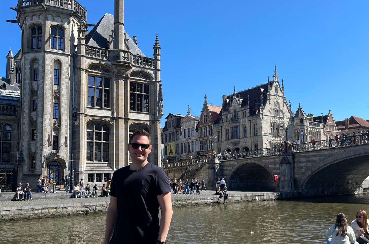 a photo of a tourist posing in Ghent, with St. Michael’s Bridge visible in the background, Ghent, Belgium? Photo by Next Level of Travel