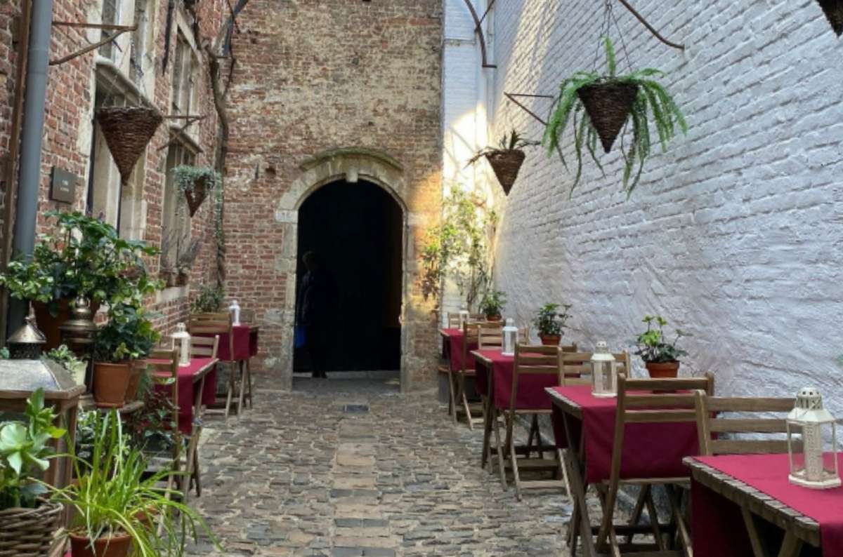 Charming narrow alley of Vlaaikensgang with red-tableclothed outdoor seating in Antwerp, Belgium