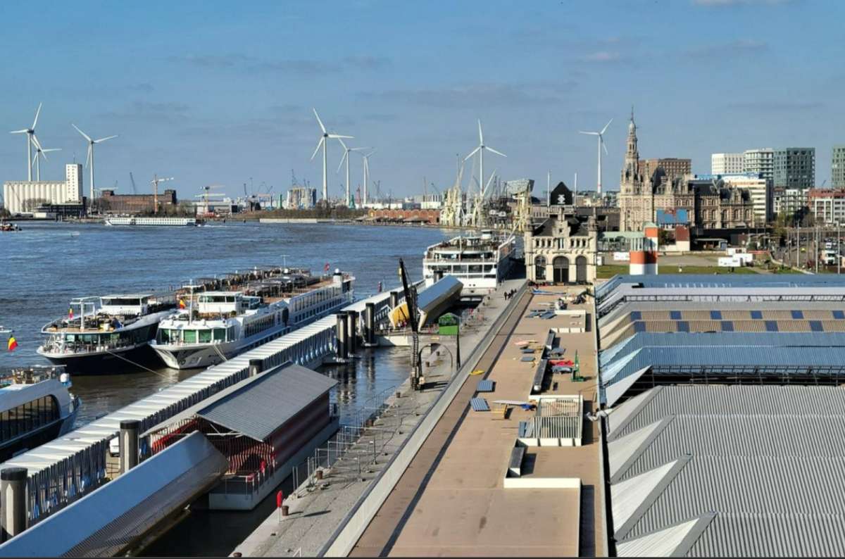 View of cruise ships docked along the Scheldt River near Het Steen fortress in Antwerp, Belgium, with wind turbines and city buildings in the background