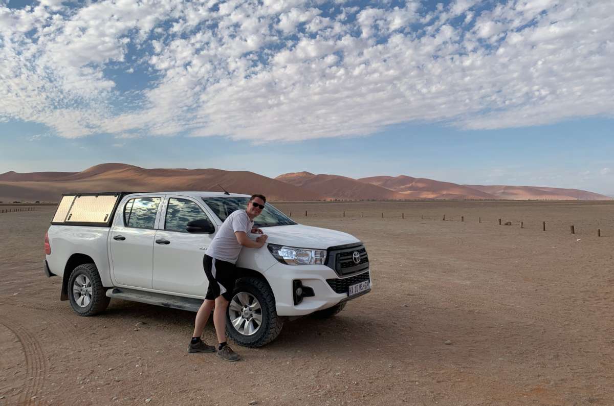 a photo of a tourist posing with a 4x4 in the middle of the Namib desert, Namibia, photo by Next Level of Travel