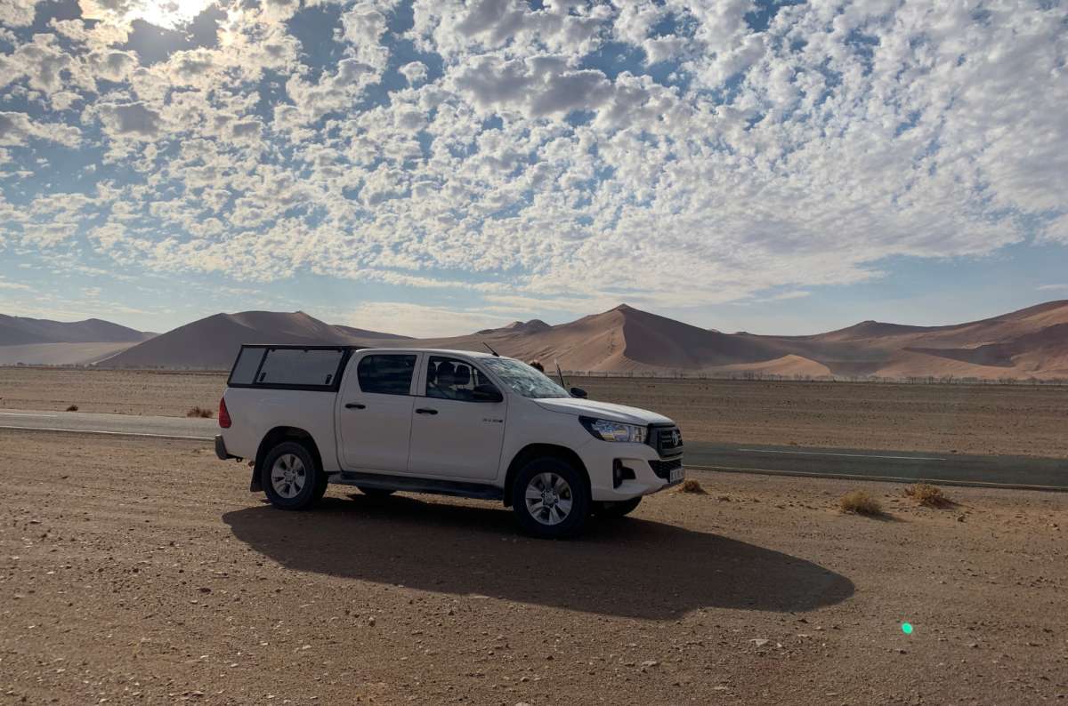 a photo of a white 4x4 car standing near the road in the Namib desert with sand dunes in the background, Namibia, photo by Next Level of Travel