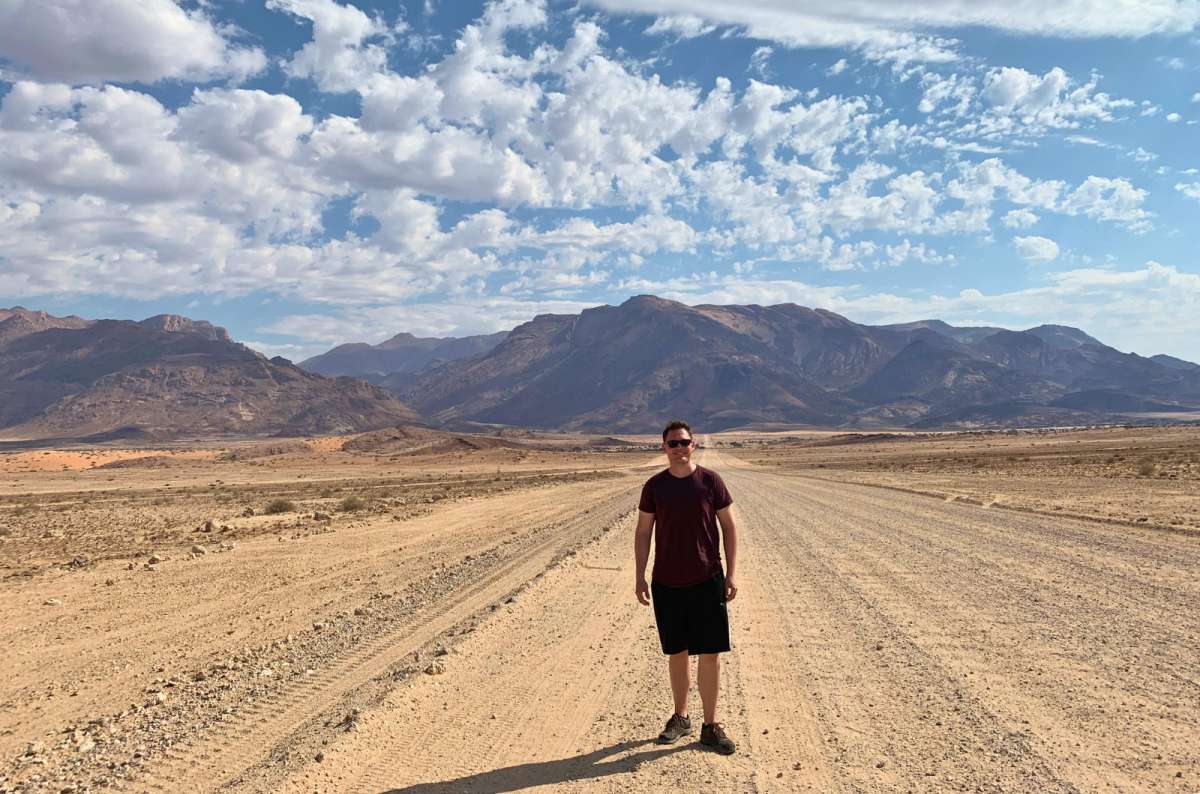 Tourist standing on a desert road with Brandberg Mountain in the background, Damaraland, Namibia, photo by Next Level of Travel