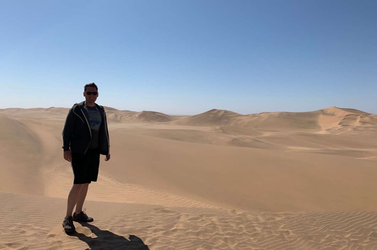 a photo of a tourist posing on top of Dune 7 near Swakopmund in Namibia, with endless sand dunes stretching into the horizon, photo by Next Level of Travel
