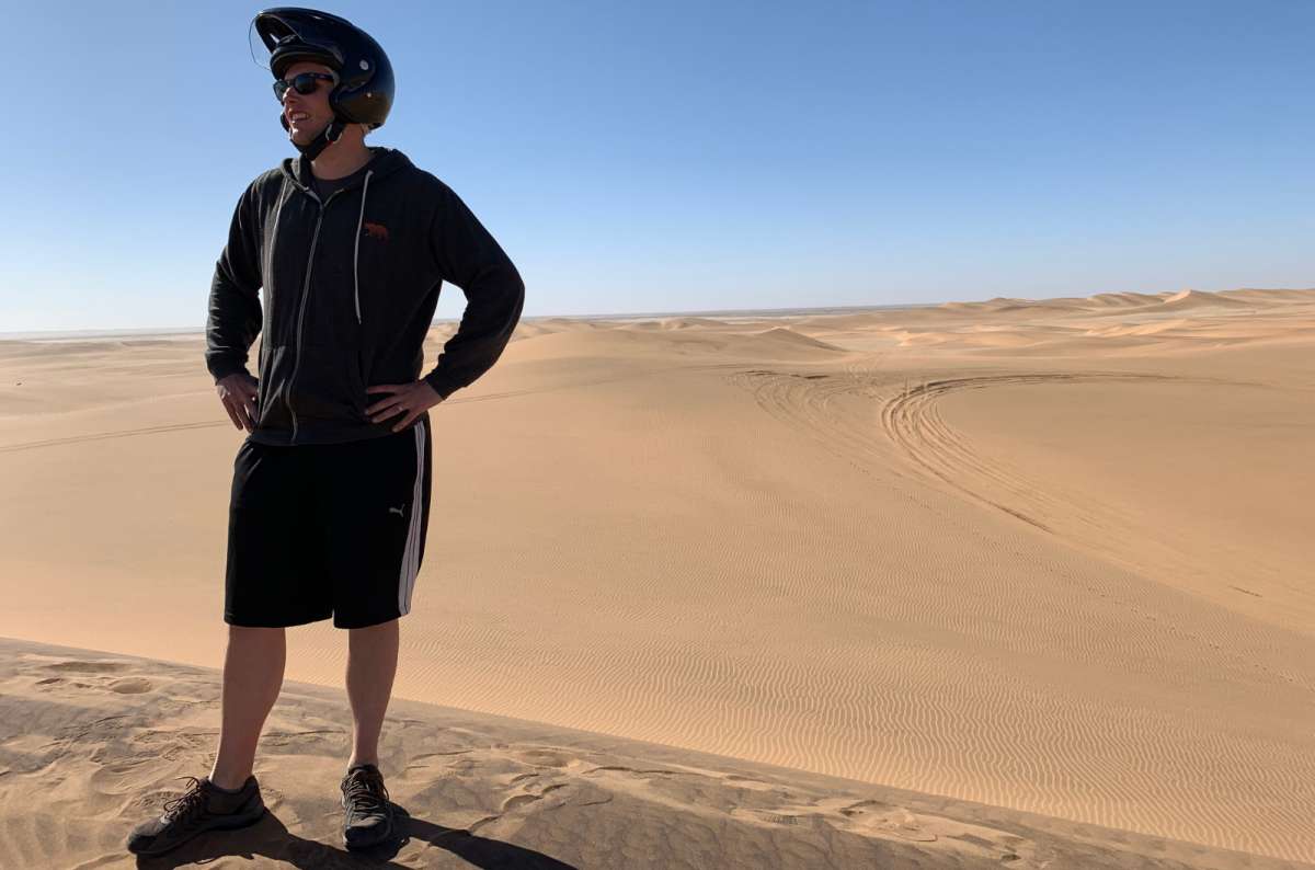 a photo of a tourist posing in the middle of the Namib Desert with a helmet after quad biking, Namibia, photo by Next Level of Travel