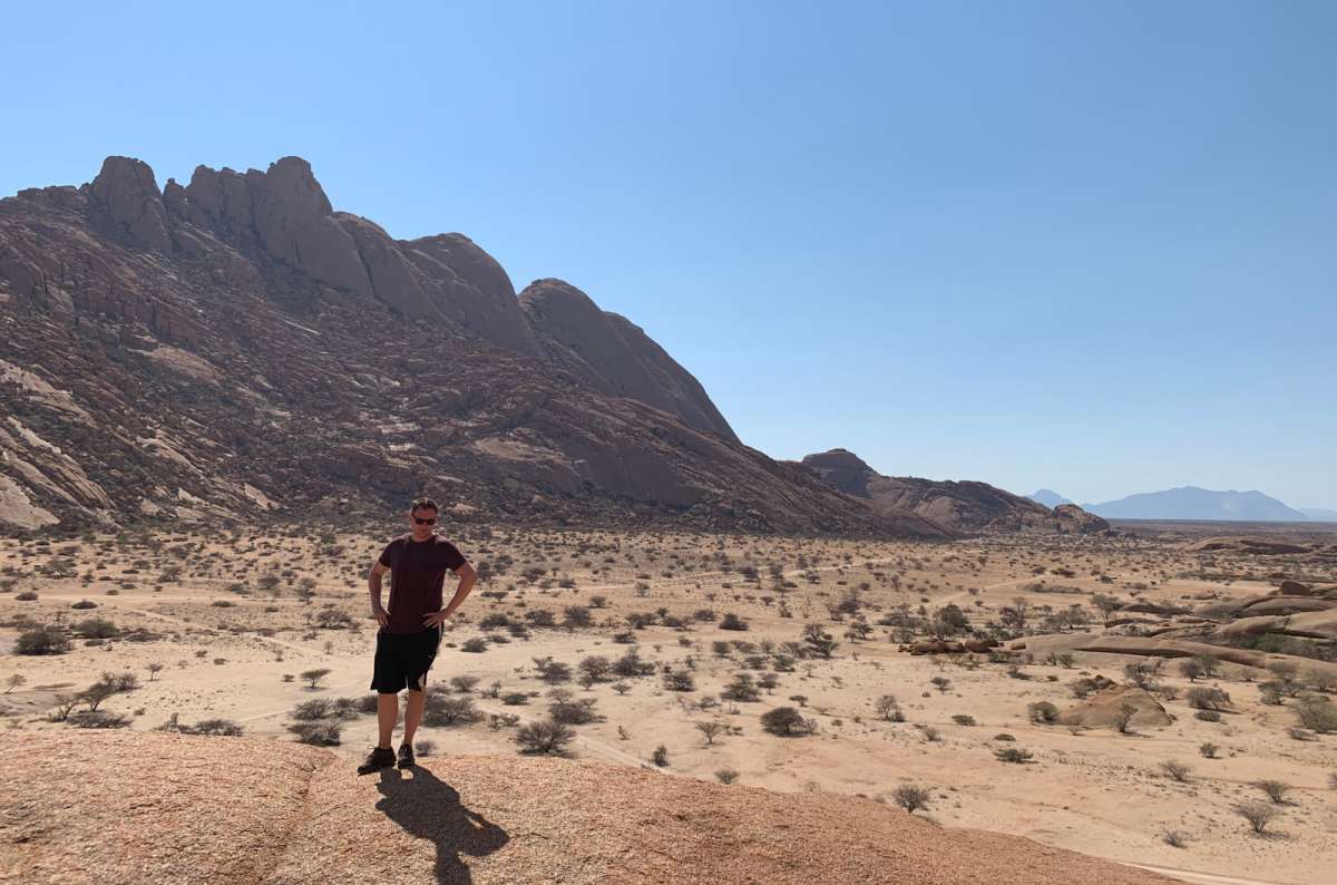a photo of a tourist posing in the middle of the Namib desert with the mountains visible in the background, Namibia, photo by Next Level of Travel