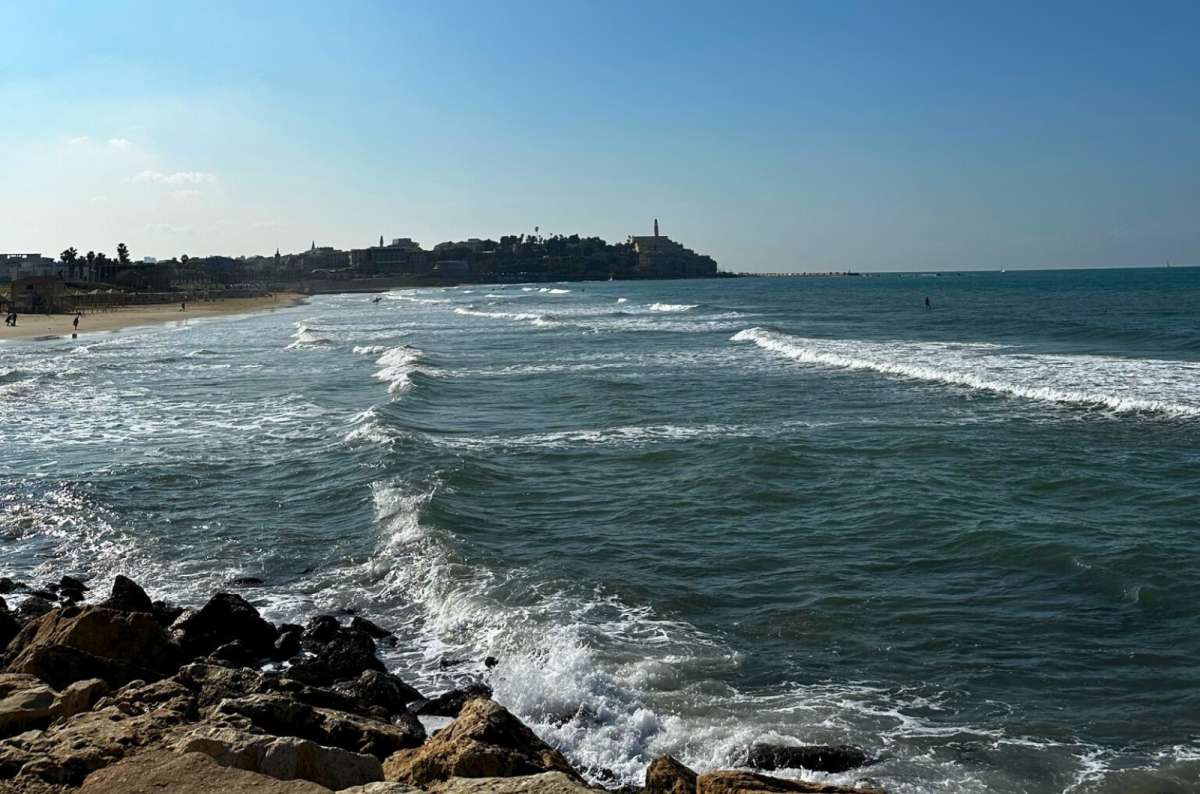Waves along the Mediterranean coastline in Tel Aviv, Israel with a view toward the Old Jaffa skyline on a clear day, photo by Next Level of Travel