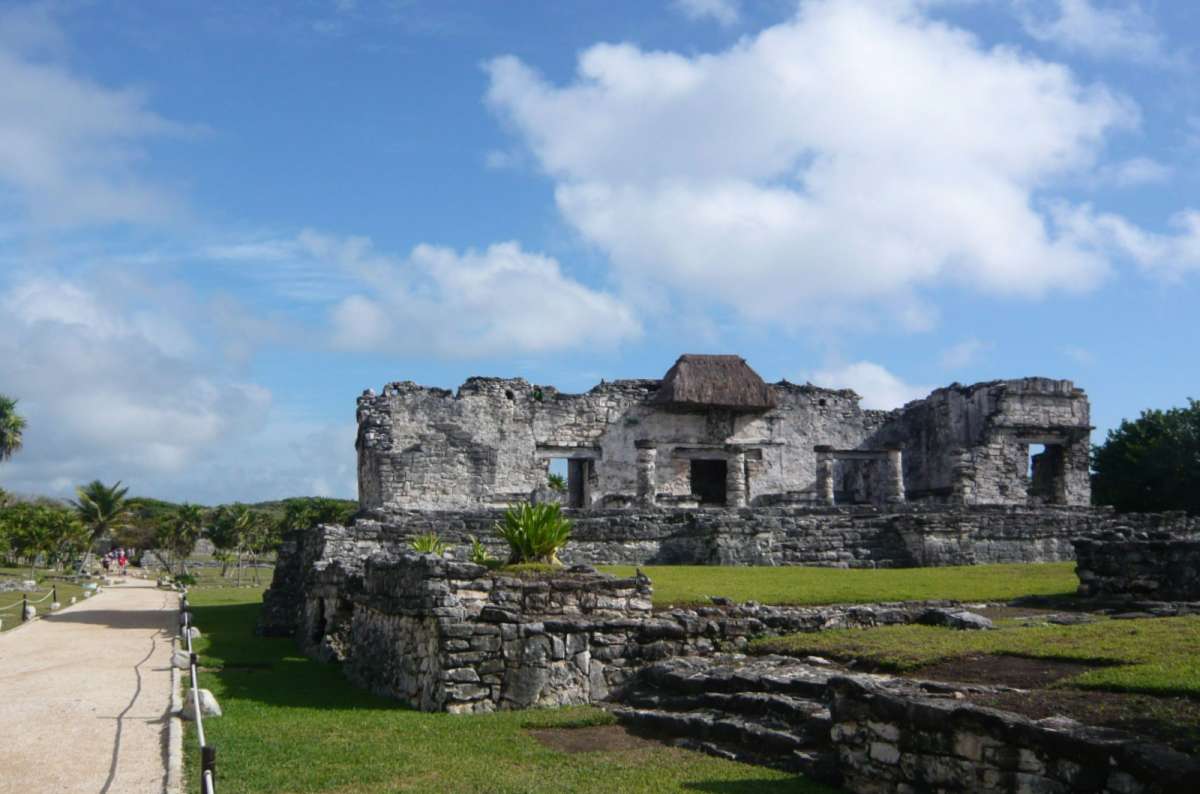 Ancient Mayan ruins of Tulum perched on cliffs above the Caribbean Sea on the Yucatán Peninsula, Mexico, with stone structures, green grass, and a coastal path under a blue sky