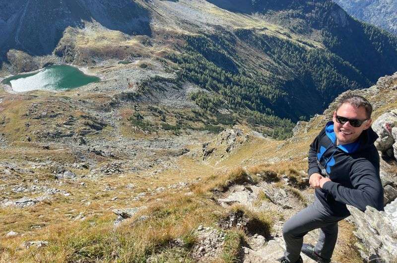A man hiking up a rocky trail on Graukogel hike, with a lake visible below, best hikes in Austria, photo by Next level of travel