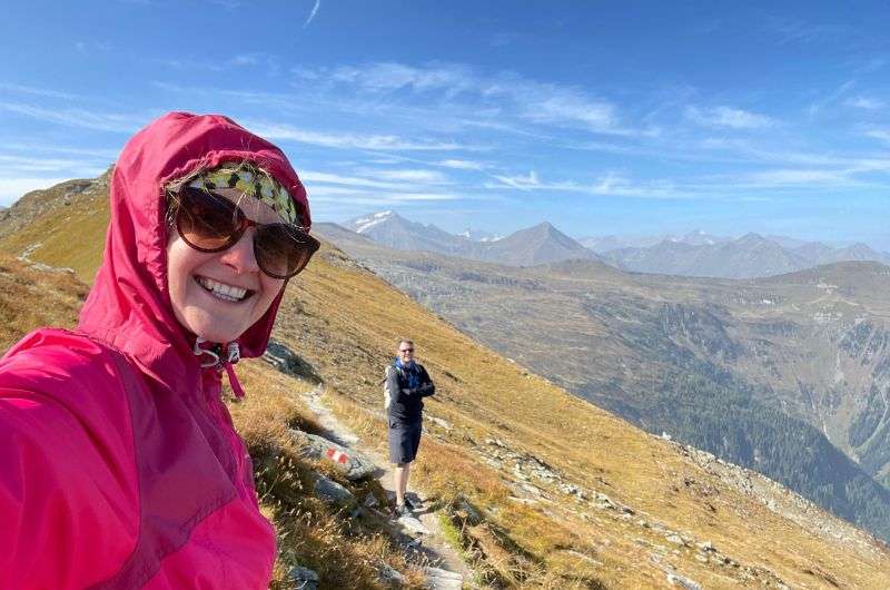 A woman in a pink jacket and a man in a backpack hiking on a scenic trail in the Austrian Alps, with mountain views in the background, hiking in Bad Gastein, Austria, photo by Next level travel